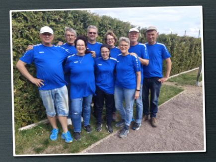 Vor einer grünen Hecke stehen neun Personen, die alle blaue T-Shirts tragen.